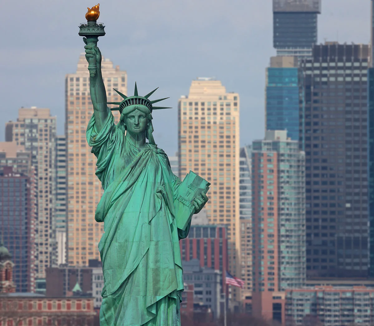 The Statue of Liberty stands proudly against a backdrop of modern skyscrapers, holding a torch and a tablet. - Out of Town in New York, NY